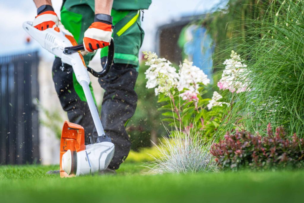 Man in professional lawn care outfit trimming a lawn edge with a string trimmer in Doral FL
